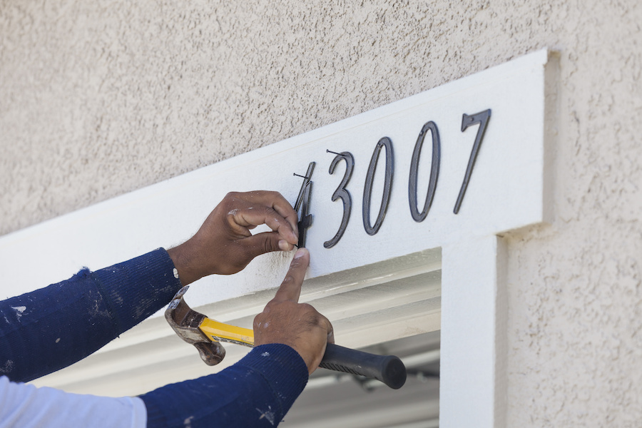 House Painter Contractor Nails Address Numbers onto House Facade.